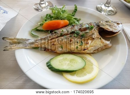 Roasted sea fish on a white plate in greek restaurant on coast peninsula Halkidiki.