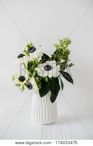 Elegant bouquet of anemones in a vase on table in white room interior, floral home dcoration