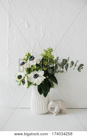 Elegant bouquet of anemones in a vase on table in white room interior, floral home dcoration