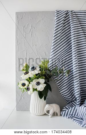 Still-life with an elegant bouquet of anemones in a vase on table in white room interior, floral home dcoration