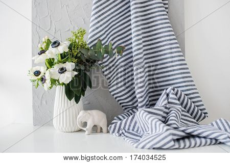 Still-life with an elegant bouquet of anemones in a vase on table in white room interior, floral home dcoration