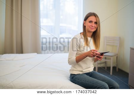 Young smiling woman sitting in the bed at home and connecting with a tablet, relax and leisure concept.