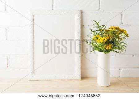 White frame mockup with wild rich golden yellow flowers in vase near painted brick walls. Empty frame mock up for presentation design. Template framing for modern art.