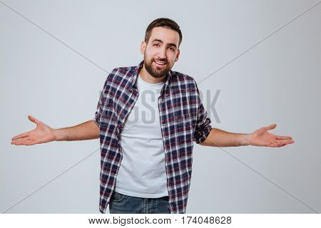 Uncomprehending Bearded man in shirt with hand to the sides which looking at camera. Isolated gray background