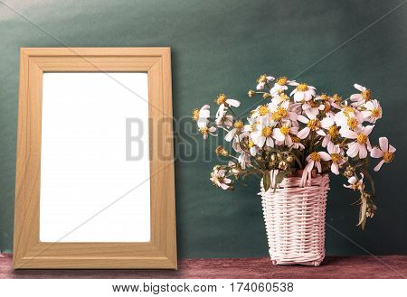 blank wooden frame mockup with basket of chamomile flowers and cactus on wooden table and brown paper wall in vintage tone.