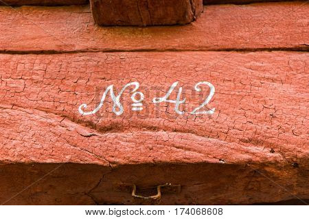 Number 42. wooden beam with cracked red paint and white Gothic numerals written No 42
