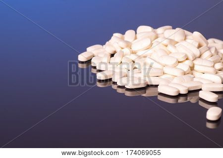 A pile of white pills is isolated on a shiny black blue background