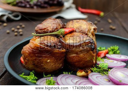 Juicy pork medallions wrapped in bacon serve on the iron pan on the dark wooden dackground. Close up