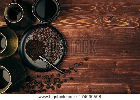 Hot coffee in black cup and turkish pots cezve with beans saucer with copy space on brown old wooden board background top view. Rustic style.