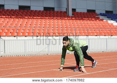 Middle Eastern male athlete ready to start running on stadiums sprint track
