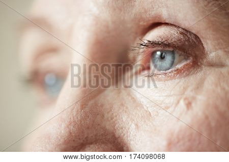 Sad blue-grey eyes of elderly woman looking to the side, extreme close-up shot