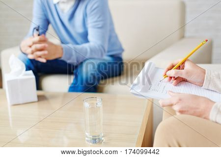 Close-up shot of female hands of psychologist making necessary notes in medical card with pencil during therapy session