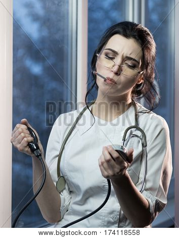 Brunette sassy female nurse in uniform smoking a cigarette measures the blood pressure