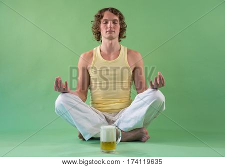 Peaceful young man doing yoga and meditation with mug of beer
