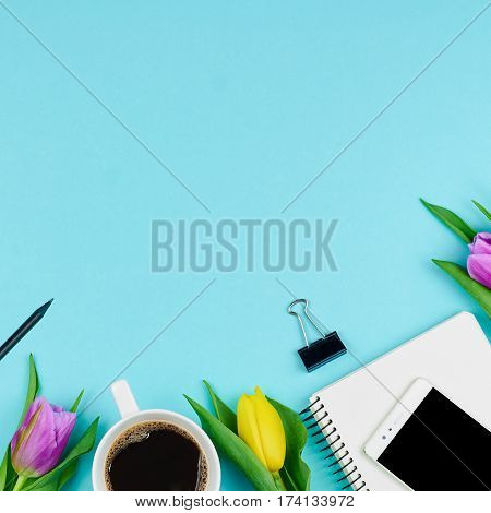 Top view of spring workplace. Work desk with notebook phone coffee and flowers. Cllose-up of working accessories with tulips
