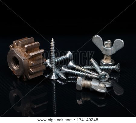 two bolts with butterfly nut rusted gear and pile of wood screws on reflected black background