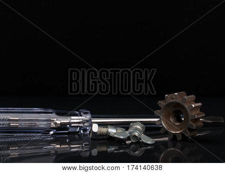 bolts with wingnut rusted gear and screwdriver with transparent handle on reflected black background