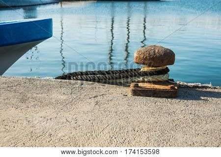 Rusty mooring bollard with tied lines at waterfront blue boat stern mediterranean Spain Costa Blanca