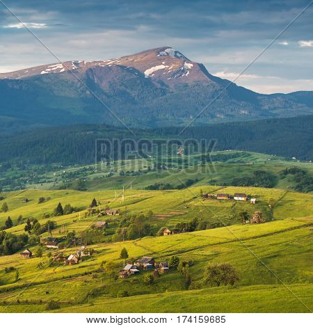 Warm evening light lies on a spring village hills under Hoverla the highest mountain of Ukraine