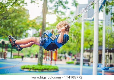 Lovely Blond Little Boy On A Swing In The Park. Adorable Boy Having Fun At The Playground