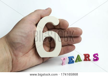 Hand holding number six on white background.