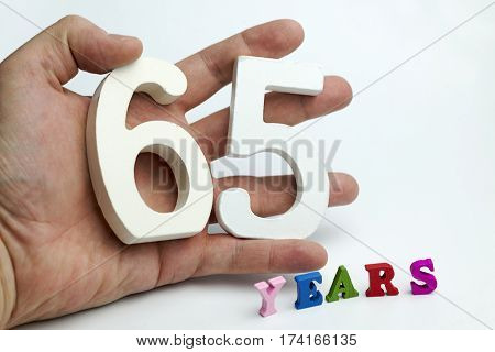 Hand holds a figure of sixty-five on a white background.