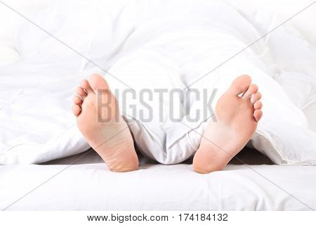 Men's feet under a white warm blanket
