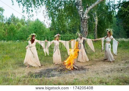 Four attractive Women with Wreath of Flowers dancing around bonfire. Ivan Kupala Holiday Celebration. Russia