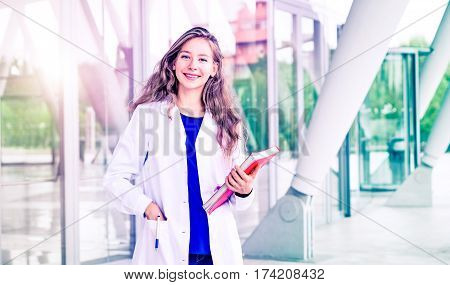 Young woman dentist student standing with positive attitude smiling at camera - Beautiful female doctor scientist looking happy and professional on modern clinic background - Medical concept