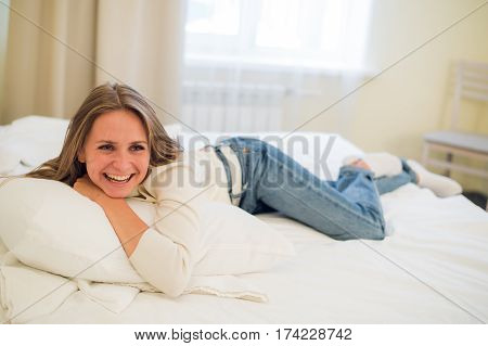 Smiling thoughtful pretty woman lying in bed at home.