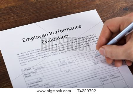 High Angle View Of A Person Filling A Performance Evaluation Form Of Employee