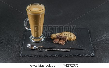 aromatic coffee latte with chocolate chunks and crispy buttered biscuits with a spoon and forks the whole on a black stone plate sweet set