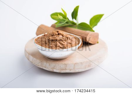 Ayurvedic Chandan powder or sandalwood paste in silver bowl with sticks and leaves placed over sahan or sahana or circular stone base for creating paste