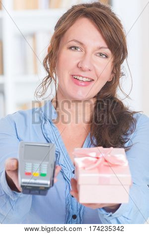 Smiling woman seller gives payment terminal and goods to the client to pay for
