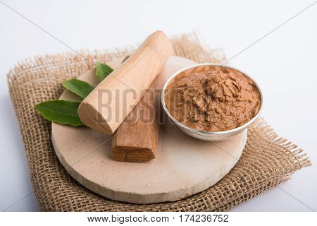 Ayurvedic Chandan powder or sandalwood paste in silver bowl with sticks and leaves placed over sahan or sahana or circular stone base for creating paste