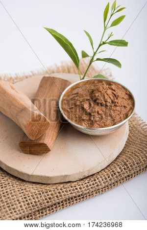 Ayurvedic Chandan powder or sandalwood paste in silver bowl with sticks and leaves placed over sahan or sahana or circular stone base for creating paste