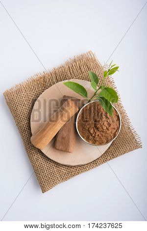 Ayurvedic Chandan powder or sandalwood paste in silver bowl with sticks and leaves placed over sahan or sahana or circular stone base for creating paste