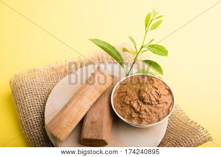 Ayurvedic Chandan powder or sandalwood paste in silver bowl with sticks and leaves placed over sahan or sahana or circular stone base for creating paste