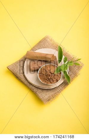 Ayurvedic Chandan powder or sandalwood paste in silver bowl with sticks and leaves placed over sahan or sahana or circular stone base for creating paste