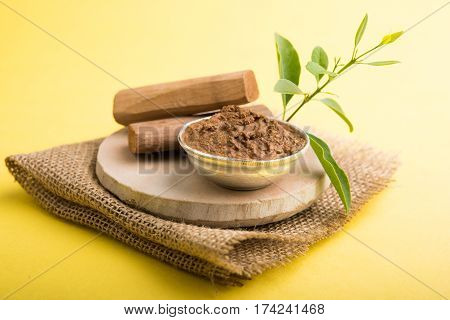 Ayurvedic Chandan powder or sandalwood paste in silver bowl with sticks and leaves placed over sahan or sahana or circular stone base for creating paste