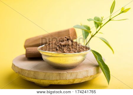 Ayurvedic Chandan powder or sandalwood paste in silver bowl with sticks and leaves placed over sahan or sahana or circular stone base for creating paste
