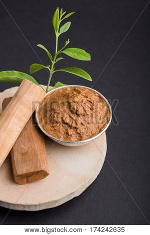 Ayurvedic Chandan powder or sandalwood paste in silver bowl with sticks and leaves placed over sahan or sahana or circular stone base for creating paste