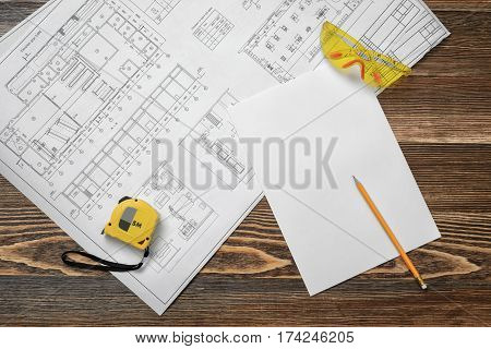 Blueprints, pencil, protective glasses, steel tape, pencil and white paper lying on wooden table background. Construction and renovation. Workers and foremen. Engineering supplies.