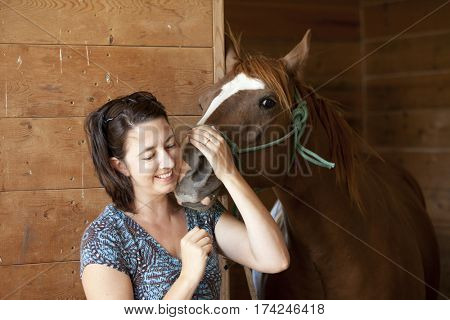Woman smiling while holding horse in barn