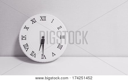 Closeup white clock for decorate show half past six or 6:30 a.m. on white wood desk and wallpaper textured background in black and white tone with copy space
