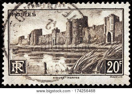 LUGA RUSSIA - FEBRUARY 7 2017: A stamp printed by FRANCE shows view of medieval city walls surrounding the Aigues-Mortes town circa 1941