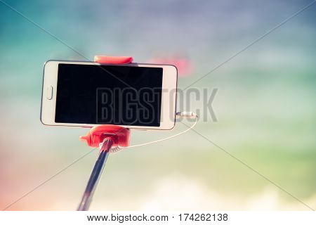 taking picture by smart phone selfie stick on blurred beautiful at beach background Vacation concept