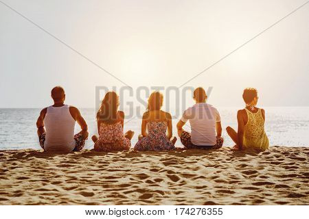 Group of five friends relaxig on sunset beach. Space for text