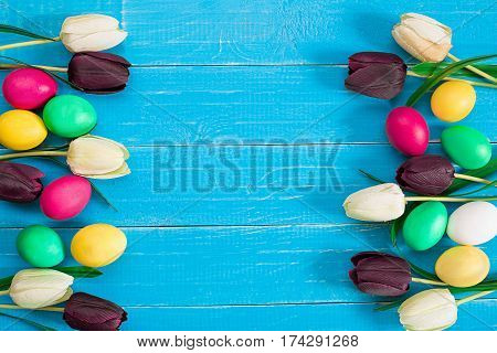 colorful easter eggs and bouquet of tulips on wooden background with space for a text, top view