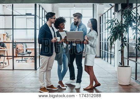 Quick meeting. Full length of young business people in smart casual wear working together and smiling while standing in the office hallway
